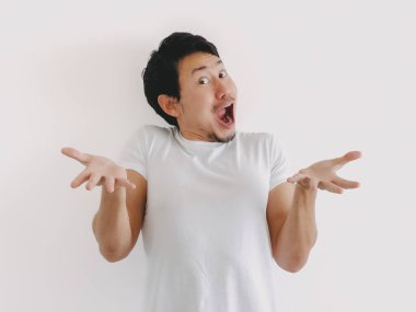 Taylandlı erkek, etkileyici bir yüz ifadesiyle şaşkınlık ve şaşkınlık gösteriyor, düz duvara yaslanırken dramatik bir şekilde ellerini kaldırıyor.