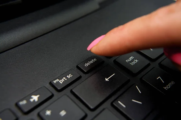 Female finger presses delete button on black laptop