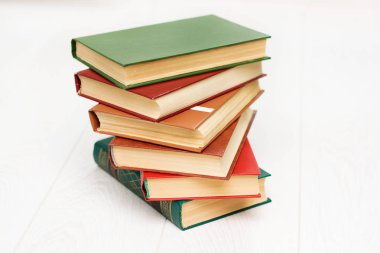 Kitap yığını beyaz ahşap bir masanın üzerinde yatıyor. Yeşil, kırmızı ve kahverengi kapaklar.