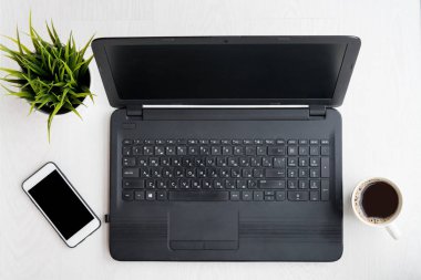 Laptop bilgisayarı, dizüstü bilgisayarı, telefonu, kahvesi ve bilgisayarı siyah ekranlı bitkisi olan modern beyaz masa. Düz yatıyordu