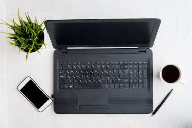 Laptop bilgisayarı, dizüstü bilgisayarı, telefonu, kahvesi, siyah ekranlı kalem ve bitkisi olan modern beyaz masa. Düz yatıyordu