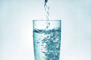 Köpüklü bir şişeden arıtılmış içme suyu dökmeye ve beyaz bir zemine sıçramaya yakın.