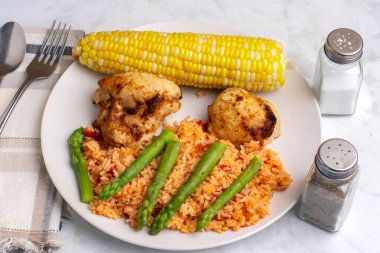 Baharatlı tavuk budu ve kuşkonmaz ve mısırla servis edilen doğranmış domates.