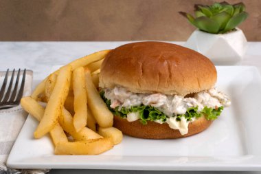 Çöreğin üzerinde patates kızartmasıyla servis edilen marullu karides deniz ürünleri salatası.