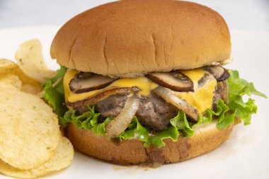 Peynirli burger, soğanlı ve mantarlı. Patates cipsiyle servis edilen bir çörek., 