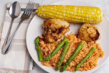 Baharatlı tavuk budu ve kuşkonmaz ve mısırla servis edilen doğranmış domates.
