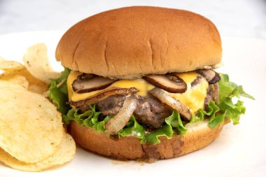 Peynirli burger, soğanlı ve mantarlı. Patates cipsiyle servis edilen bir çörek., 