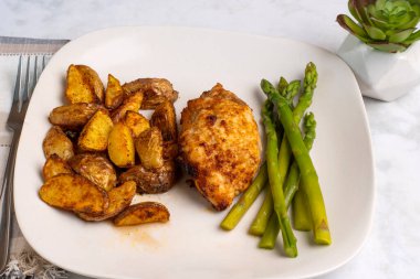 kuşkonmaz ve patates dilimleri ile servis edilen tavuk budu.