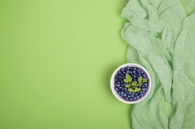 Yeşil zemin üzerine bir kase yeşil yaprakları ile taze yaban Yaban mersini. Üstten görünüm.