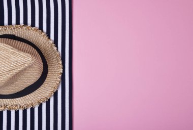 Çizgili kıyafetler ve pembe bir arka plan üzerinde hasır şapka. Üstten görünüm. Düz yatıyordu.