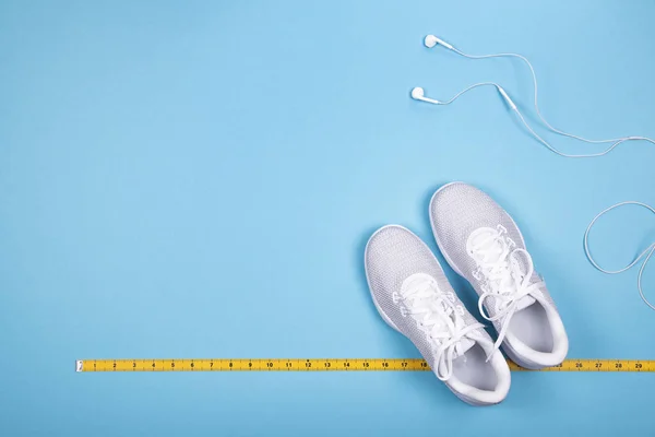 White sneakers with yellow measuring tape and white earphones (headphones)  
on blue background.