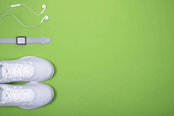 White sport shoes (sneakers) with smart watch (activity tracker) and earphones (headphones) on green color background. — Stock Photo, Image