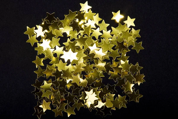 Sparkling and holographic golden star confetti on black background.