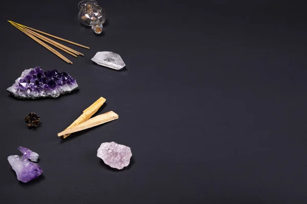 Amethyst and quartz crystal stones, palo santo wood, aromatic sticks, cone and decorative bottle on black background.