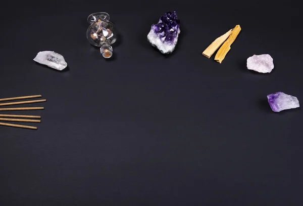 Amethyst and quartz crystal stones, palo santo wood, aromatic sticks and decorative bottle on black background.