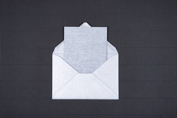 Срібна сіра порожня картка у відкритому конверті на темному текстурованому фоні . — стокове фото