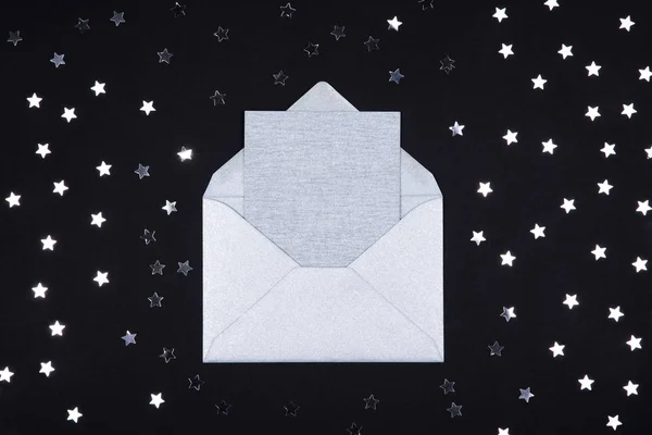 Tarjeta en blanco gris plateado en sobre abierto sobre fondo negro decorado con confeti estrella . —  Fotos de Stock