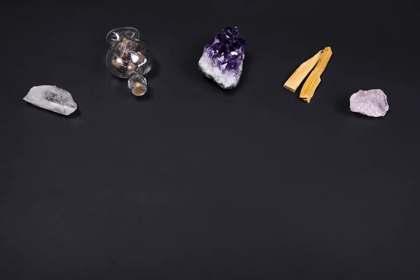 Amethyst and quartz crystal stones, palo santo wood and decorative bottle on black background. — Stock Photo, Image