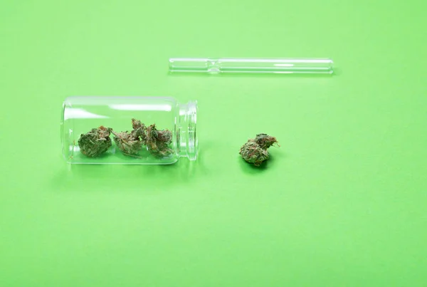 Brotes secos de marihuana medicinal en una botella de vidrio con tubo sobre fondo verde . — Foto de Stock