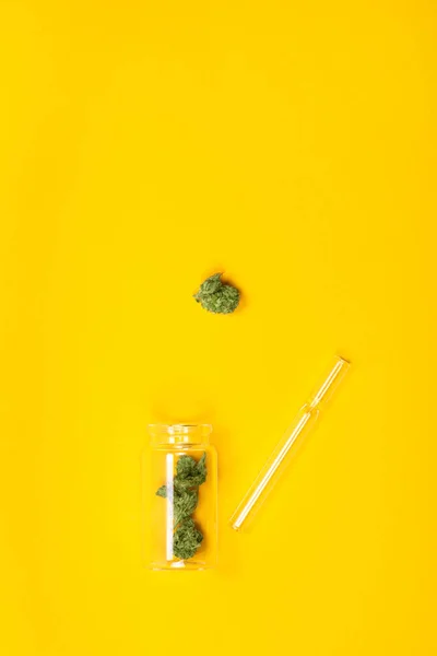 노란 배경에 파이프와 유리 병에 말린 된 의료 대마초 싹. — 스톡 사진
