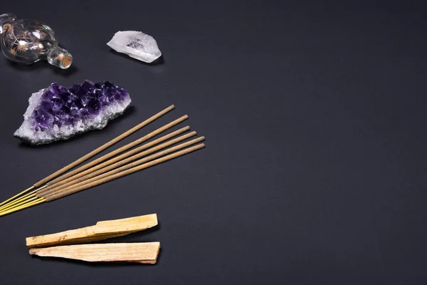 Ametist ve kuvars kristal taşlar, palo santo ahşap, aromatik sopa ve siyah arka plan üzerine dekoratif şişe.