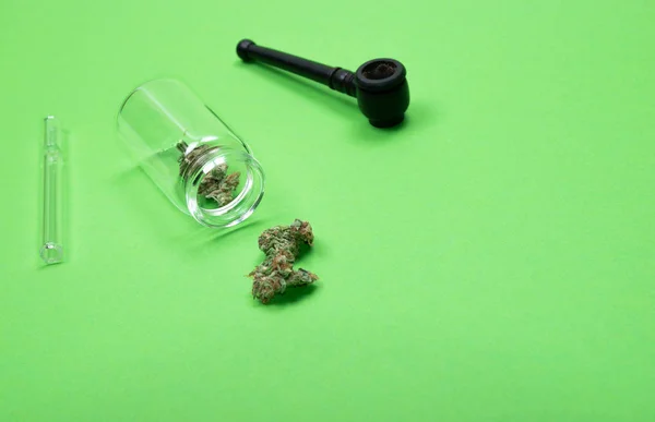 Brotes secos de marihuana medicinal en una botella de vidrio con tubos de madera y vidrio sobre fondo verde . — Foto de Stock