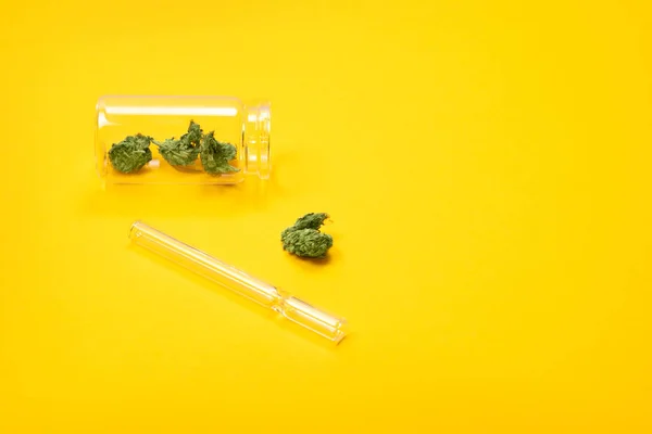 Secco germogli di marijuana medica in una bottiglia di vetro con tubo su sfondo giallo . — Foto Stock