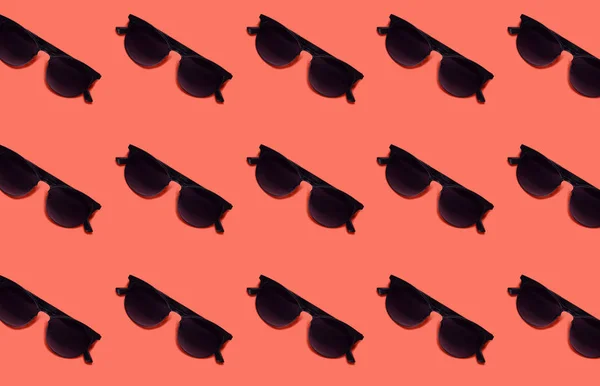 Yaz desen mercan renk arka plan üzerinde siyah güneş gözlüğü ile yapılan. Minimal tatil, yaz veya moda moda kavramı.
