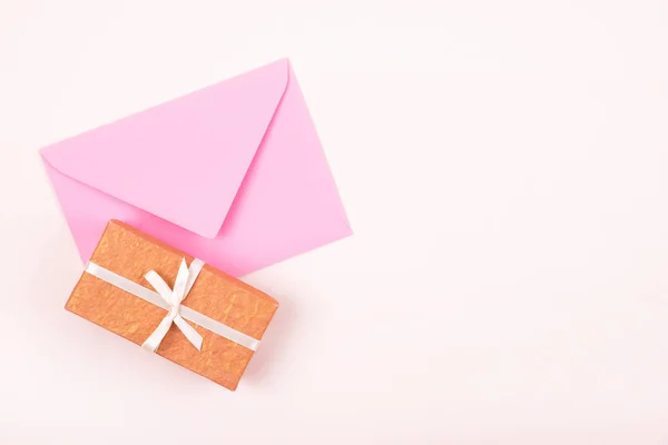 Проста подарункова коробка, прикрашена білою стрічкою та рожевим конвертом на пастельному тлі. Плоский прошарок . — стокове фото