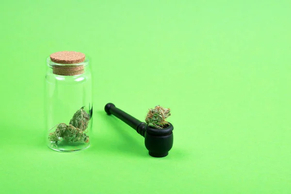 Brotes de marihuana médica seca en una botella de vidrio con tubo de madera sobre fondo verde . — Foto de Stock