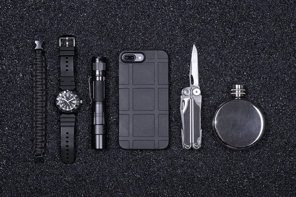 Vardagliga Carry (EDC) militära objekt för män-Multi Tool, lättare, mobiltelefon i skydds fallet, taktisk klocka, överlevnad armband, ficklampa och kolv Blackstone (mineraler) smula bakgrund. — Stockfoto