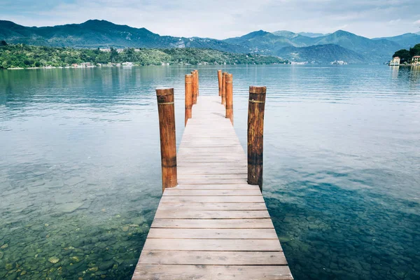 Yeşillikdağ arka plan ile Orta San Giulio Gölü üzerinde ahşap iskele. İtalya.