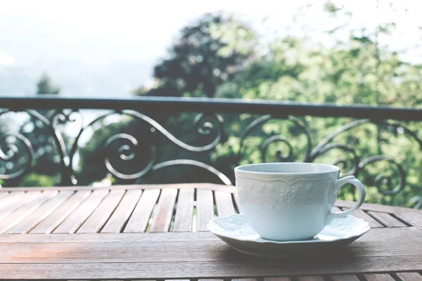 Taza de té de cerámica blanca sobre un platillo sobre una mesa de madera sobre un fondo pintoresco . — Foto de Stock