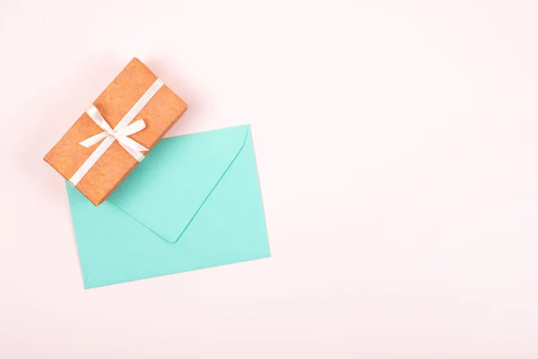 Eenvoudige gift box versierd met witte striklint en turquoise envelop op pastel roze achtergrond. Platte lay. — Stockfoto