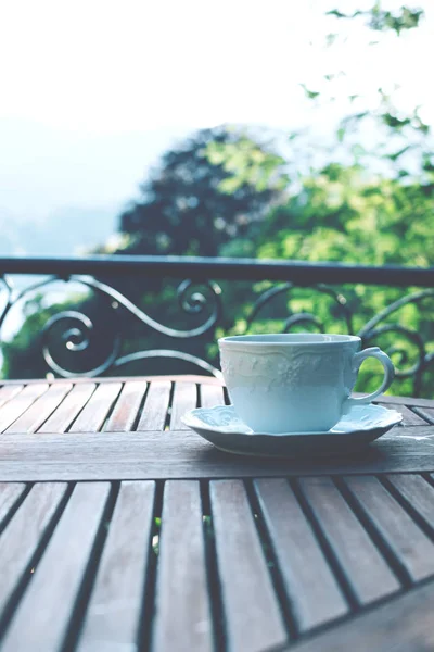 Λευκό κεραμικό φλιτζάνι τσάι σε ένα πιατάκι σε ξύλινο τραπέζι στο γραφικό φόντο. — Φωτογραφία Αρχείου