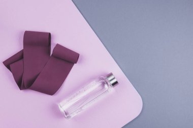 Kestane rengi genişletici elastik bant, pembe yoga minderinin üzerinde yeniden kullanılabilir cam su şişesi ve tarafsız gri arka plan. Yoga pilates ya da fitness pratiği. Kilo verme ve spor konsepti. 