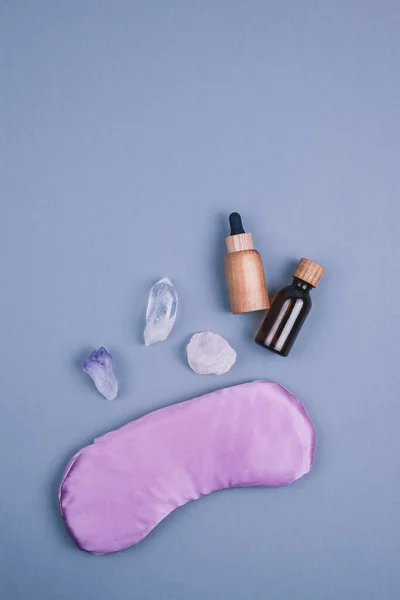 Değerli taş kristal minerallerin üst görüntüsü, mor göz yastığı, cam ve gri arka planda gerekli yağlar için ahşap şişeler. Mesaj için yer. Rahatlama ve meditasyon kavramı.