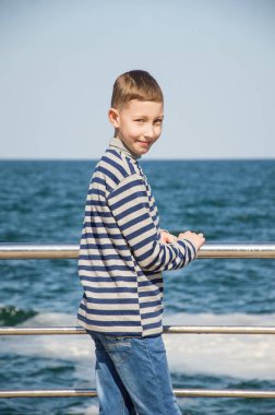 Rıhtımda duran çocuk. Arka plan olarak Mavi Deniz ve mavi gökyüzü. 