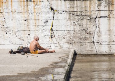 Tekerlekli sandalyeli yaşlı adam bahar güneşinde güneşleniyor. İskelede çimento levhalar. Odessa, Ukrayna, Nisan 2019.