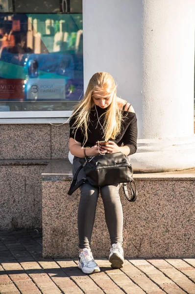 The girl sits on the ledge of the building and looks at the phon — Stock Photo, Image