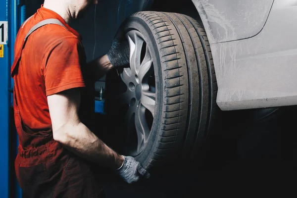 A mechanic in the service center checks the suspension of the dirty car. Performs seasonal wheel replacement.