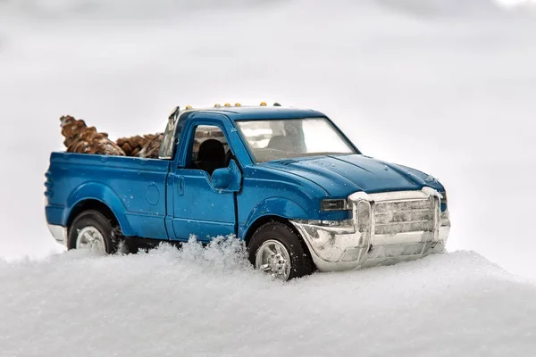Blue toy pickup truck in sawmill. Stuck at snowdrift and sawdust. Carrying fir cones in the back of a car body.