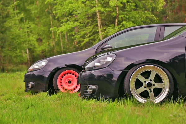2 black cars in tuning. Parked on grass. With custom polished wheels, and living coral color wheel.