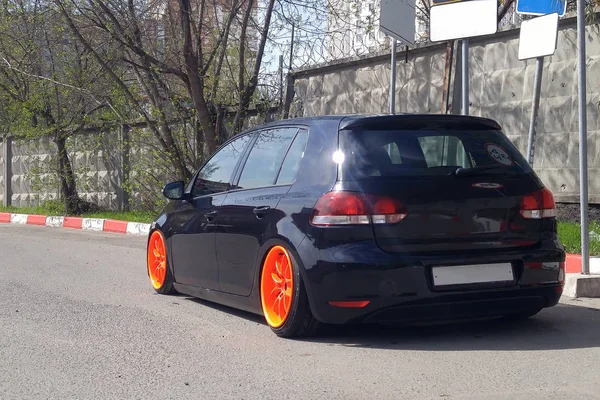 Black hatchback with orange wide wheels tuned by air suspencion parked under different road signs. Stance car