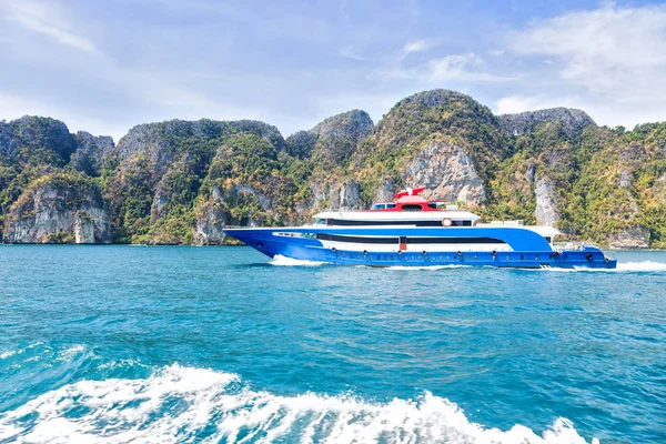 Blue with white and red accents pleasure speed boat. Sailing on the sea against a tropical mountain island. Side view. Motor track and waves on the water.