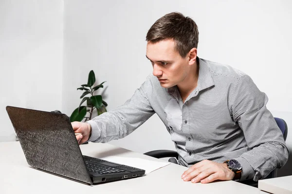 Worry businessman using laptop while sitting in office. Indicates a pen on the screen, reads important documents.