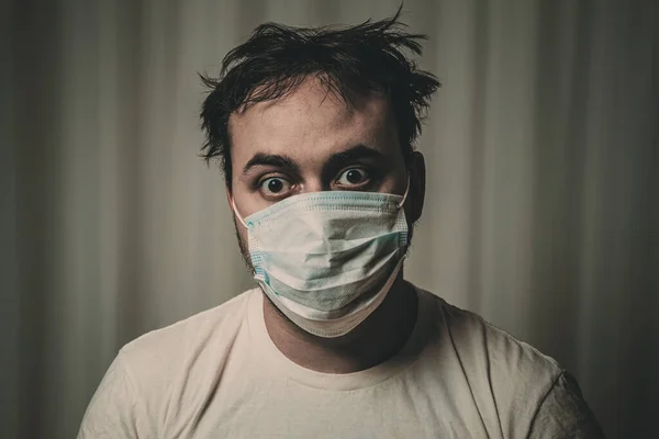 Unshaven man in a medical mask with tousled hair looking at the camera. On white background. Image toned in gloomy tones. dark, depressing.