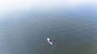 Calm waters at midday with a lone paddleboard gliding smoothly over the serene lake surface. High quality photo