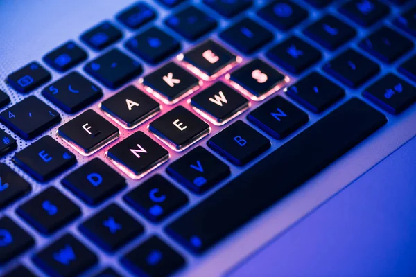 Fake News auf einer hinterleuchteten Tastatur in blauem Umgebungslicht — Stockfoto