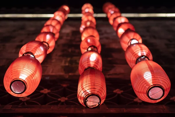 Gruppe roter chinesischer Laternen, die nachts an einer beleuchteten Wand hängen — Stockfoto